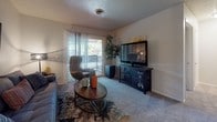 Located at 4101 SW 45th Ave in Amarillo, Texas, this single-floor residence offers a thoughtfully designed layout with a cohesive, eclectic aesthetic throughout. The living area serves as the heart of the home, featuring plush carpeting, a sliding glass door that invites natural light and provides access to an outdoor balcony area, and a decorative world map as a focal point above the sofa. A wingback accent chair adds a sophisticated touch, while a round wooden coffee table anchors the space. An adjacent dining area accommodates a round table with metal-framed chairs beneath a globe pendant light, accented by botanical wall art. The kitchen is outfitted with rich dark wood cabinetry, dark granite-style countertops, hardwood-style flooring, and black appliances including a gas range and built-in microwave. The bedroom is carpeted and features a tufted upholstered bed frame, bold abstract artwork, and a window with vertical blinds. The bathroom includes a clean, white-tiled tub and shower combination with brushed nickel fixtures. Textured ceilings are present throughout, and the overall interior palette of warm neutrals accented with pops of orange, teal, and gold gives the space a vibrant yet inviting character.