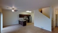 This two-story home offers a functional and well-organized layout across its main and upper levels. The main floor showcases an open-concept design that seamlessly connects the living area and kitchen, creating a spacious and cohesive environment. Light hardwood-style flooring extends throughout the main level, lending a clean, contemporary feel to the space.

The kitchen is a standout feature, equipped with stainless steel appliances including a range, microwave, and refrigerator. Rich dark cabinetry provides ample storage and creates a striking contrast against the light-toned countertops and walls. A peninsula with an integrated sink and breakfast bar adds both practicality and a casual dining option. Recessed lighting above the kitchen ensures the workspace is well-lit.

The adjacent living area is open and airy, benefiting from a ceiling fan that enhances comfort and airflow. Neutral white walls throughout create a bright, versatile backdrop. A staircase along one wall leads to the upper floor, contributing to the efficient use of space on the main level. Floor vents are visible, indicating a central HVAC system for climate control throughout the home.