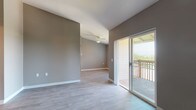 This single-floor unit is designed with a practical and open layout, highlighted by a spacious living area with vaulted ceilings and light-toned hardwood-style flooring. A ceiling fan provides year-round comfort, and built-in shelving along one wall offers convenient storage and display space. Sliding glass doors open directly onto a wood-railed balcony, presenting sweeping panoramic views of the surrounding tree-lined neighborhood and distant mountains beneath an expansive sky.

The galley-style kitchen runs parallel along both walls, featuring white cabinetry with wood trim, laminate countertops, a full suite of white appliances including an electric range and refrigerator, and a double sink. In-unit laundry connections are also visible at the rear of the kitchen. The kitchen connects seamlessly to the main living and dining areas.

Two bedrooms are finished with wall-to-wall carpet and neutral gray-toned walls, each receiving natural light through windows with vertical blinds. The full bathroom includes a tub-shower combination, a single-sink vanity with storage cabinetry, a granite-style countertop, and hardwood-style flooring consistent with the rest of the unit. The overall palette of warm grays and white trim gives the space a clean, cohesive aesthetic throughout.