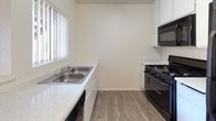 Located at 23215 Ironwood Ave, Unit 17 in Moreno Valley, CA, this single-story residence offers a clean, functional layout designed for comfortable everyday living. The living area is finished with plush wall-to-wall carpeting and features a sliding glass door that opens to a private balcony, allowing natural light to fill the room and providing pleasant views of the surrounding greenery. A front entry door leads directly into this open living space, which connects seamlessly to the kitchen area. The kitchen is equipped with light-toned quartz-style countertops, a double-basin stainless steel sink, white cabinetry, wood-look vinyl flooring, and black appliances including a gas range and built-in microwave. The bedrooms are carpeted and well-lit by natural light through windows that overlook outdoor landscaping. Closet space is provided in the bedrooms for practical storage. Two bathrooms serve the unit, each featuring a shower-tub combination, toilet, and vanity with countertop sink. One bathroom includes wood-look vinyl flooring and a small window for ventilation, while the other features a similarly clean, all-white finish. Textured ceilings are consistent throughout, contributing to the unit's straightforward and neutral aesthetic.