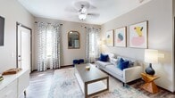 This modern apartment offers a well-designed 780 sq ft floor plan with 2 bedrooms and 2 bathrooms. The open-concept living area showcases a sleek kitchen with dark wood cabinetry, stainless steel appliances, and a breakfast bar with chic seating. The living room features a comfortable grey sofa, abstract wall art, and large windows with patterned curtains. Both bedrooms are carpeted, with the 120 sq ft primary bedroom boasting a tufted headboard and en-suite bathroom. Bathrooms feature wood vanities and wood-look tile flooring. Throughout the space, a neutral color palette is accented with pops of blue, creating a cohesive and inviting atmosphere.