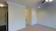 This single-floor space presents a well-maintained and classically styled interior that emphasizes clean lines and timeless finishes. The rooms are dressed with elegant crown molding that frames the ceilings, adding a refined architectural detail that elevates the overall aesthetic. Soft, neutral wall tones in a warm off-white palette create a calm and welcoming atmosphere throughout. Plush wall-to-wall carpeting in a light beige hue provides comfort underfoot and contributes to the cohesive, understated color scheme. Recessed lighting is thoughtfully integrated into the ceiling, offering practical illumination while maintaining a sleek, unobtrusive look. A ceiling fan is also present, combining functionality with comfort. Crisp white baseboards and panel-style doors with brushed hardware provide polished finishing touches that complement the interior's traditional character. The layout features connected rooms with open doorways that allow for a natural flow between spaces, with glimpses into adjoining areas suggesting a functional and well-organized floor plan. The space is move-in ready, presenting a neutral and versatile canvas well-suited to a variety of furnishing styles and personal tastes.