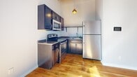 Located at 611 Madison St in Clarksville, Tennessee, this single-floor unit showcases an impressive blend of industrial character and modern finishes. Soaring ceilings with exposed ductwork and wood beam framing lend the space a loft-like aesthetic, while warm-toned hardwood flooring runs consistently throughout, creating a cohesive and inviting atmosphere.

The kitchen is well-appointed with dark espresso cabinetry, granite-look countertops, and a full suite of stainless steel appliances, including a refrigerator, electric range, and built-in microwave. A pendant light with a gold fixture adds a stylish accent above the workspace.

The main living area is generously proportioned with high ceilings and crisp white walls that amplify the natural light pouring in through large windows. These windows also offer views of the surrounding Clarksville streetscape, adding a sense of connection to the neighborhood.

The bedroom benefits from the same soaring ceiling height, large windows, and a built-in closet with bifold doors. An adjacent bathroom is visible through the doorway, fitted with clean, modern fixtures. The open layout and elevated ceiling height throughout give the entire space a sense of airiness and scale rarely found in single-floor units.