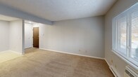 Located at 2141 Aurelius Rd in Holt, Michigan, this one-bedroom, one-bathroom unit offers a practical and comfortable single-floor layout. The living room is a generous, open space finished with wall-to-wall carpet, soft blue-gray walls, and a textured ceiling. A wall-unit air conditioner and baseboard heating sit beneath a wide window that invites natural light and outdoor views of surrounding greenery. The space flows into a dedicated entrance area, providing a clean transition into the home. The combined dining room and kitchen area offers a functional layout with room for both meal preparation and dining. The bedroom is a well-proportioned retreat featuring plush carpeting, a window with blinds for natural light and privacy, and baseboard heating. Notably, the bedroom provides access to three closets, offering exceptional storage capacity. The full bathroom is finished with classic white subway-style wall tile surrounding a tub and shower combination, lending a clean and timeless look. Neutral tones, soft carpet, and consistent blue-gray paint throughout the unit create a cohesive and calm atmosphere. A hallway connects the main living spaces efficiently, contributing to the unit's well-organized flow.