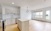 This well-designed one-bedroom, two-bathroom unit at 9660 229 St NW offers a thoughtfully arranged open-concept floor plan finished with consistent light hardwood flooring throughout. The combined kitchen, dining, and living area forms the heart of the unit, anchored by a central kitchen island with a white quartz countertop and wood-tone cabinetry. The kitchen is equipped with stainless steel appliances—including a refrigerator, range, microwave, and dishwasher—and features a classic white subway tile backsplash. A geometric pendant light fixture adds a modern design accent above the island. Large windows in the living area allow generous natural light and provide views of the surrounding neighbourhood. The bedroom is a comfortably sized retreat featuring a window with outdoor views, baseboard heating, and dual closets with panelled double doors offering ample storage. The two bathrooms are finished in a clean, contemporary style: one includes a full soaker tub with tiled surround, while the other features a wood-tone vanity with quartz countertop and a large mirror. A glazed door opening to a private outdoor area provides additional natural light to the entryway.