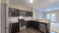 Located at 40 Hutchinson Ave in Columbus, Ohio, this well-appointed single-floor residence offers a thoughtfully designed layout with contemporary finishes throughout. The kitchen serves as a functional centerpiece, showcasing rich dark espresso cabinetry, light granite-style countertops, a classic subway tile backsplash, and a full suite of stainless steel appliances including a refrigerator, electric range, over-the-range microwave, and dishwasher. Durable wood-style flooring runs throughout the kitchen, adding warmth and easy maintenance to the space. The kitchen flows naturally into the living area, which is finished with plush carpet and features a sliding glass door that opens to a private balcony, allowing for natural light and outdoor access. The bedrooms are generously proportioned, each finished with soft neutral carpet and clean white trim. One bedroom connects directly to a private en-suite bathroom, which is outfitted with a dark vanity, granite-style countertop, a glass-enclosed shower, and matching wood-style flooring. Additional interior doors provide access to closets and utility spaces, contributing to ample storage throughout. The overall aesthetic is clean, modern, and cohesive, with a neutral color palette that creates a bright and welcoming atmosphere.