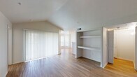 This well-appointed 2-bedroom, 2-bathroom single-floor residence offers a thoughtful layout designed for comfortable everyday living. The entryway welcomes you with light hardwood-style flooring and clean white walls that carry throughout much of the home, creating a bright and cohesive aesthetic.

The open living area is highlighted by vaulted ceilings that lend an airy sense of volume, with large vertical blinds allowing natural light to filter in generously. Built-in shelving adds functional storage and a charming architectural detail to the living space.

The modern kitchen features sleek, high-gloss white cabinetry, clean white countertops, and stainless steel appliances including a refrigerator and dishwasher. Pendant lighting and an open layout make the kitchen both practical and inviting, with a sight line connecting to the main living areas.

Both bedrooms are comfortably sized, and each is served by a full bathroom equipped with a tub and shower combination with tiled surrounds. The hallway connecting the rooms is bright and neatly proportioned.

A dedicated in-unit laundry area houses a full-size washer and dryer side by side, with additional wire shelving above for storage. Throughout the home, the combination of vaulted ceilings, natural light, and clean finishes creates a welcoming and functional living environment.