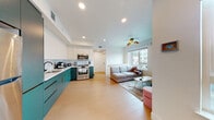 This single-floor unit in Berkeley, CA, showcases a thoughtfully designed interior with a clean, modern aesthetic throughout. The open-plan kitchen and living area form the heart of the space, anchored by a striking kitchen fitted with two-tone cabinetry — bold teal lower cabinets with gold hardware contrast against crisp white upper cabinets. Light wood-style flooring runs continuously through the space, enhancing the sense of openness, while recessed lighting provides even illumination across the area. Stainless steel appliances, including a range, microwave, and refrigerator, complete the functional kitchen setup.

The living area flows naturally from the kitchen, offering a comfortable, well-lit space with a window that frames views of the surrounding Berkeley streetscape. The bedroom is compact yet practical, featuring a large window that brings in natural light and overlooks the neighborhood.

The bathroom is a standout feature, finished with classic penny tile flooring in a black-and-white pattern. A teal vanity with gold-tone fixtures mirrors the kitchen's color palette, and an LED-backlit mirror adds a modern touch. Built-in open shelving provides convenient storage, and a full soaking tub with a shower curtain completes the well-designed space.