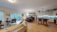 This thoughtfully designed three-floor home offers a seamless blend of functionality and style across its multiple levels. The main floor showcases an open-concept layout where the living, dining, and kitchen areas flow naturally into one another, all unified by warm hardwood flooring. Sliding glass doors in the living area lead to an outdoor deck, framing lush greenery views and filling the space with abundant natural light. The dining area features an elegant dark wood table set beneath a chandelier, complemented by a large framed mirror and classic sideboard. The kitchen is outfitted with crisp white cabinetry, under-cabinet lighting, dark countertops, stainless steel appliances, and a central island with seating for two. A dedicated home office on the main level provides a quiet retreat, complete with hardwood floors and classic furnishings. Upstairs, the spacious primary bedroom offers plush carpeting, multiple windows overlooking the surrounding trees, and a sitting area, while additional bedrooms provide comfortable accommodations with ample closet space. A well-appointed bathroom features a glass-enclosed walk-in shower with elegant subway tile. The lower level is home to a dedicated fitness room equipped with cardio machines, free weights, and wall mirrors, adding a practical wellness amenity to this versatile home.