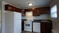 Located at 87-89 S State Street in Upper Darby, PA, this single-floor space offers a practical and functional layout designed for everyday living. The kitchen serves as a notable feature of the unit, showcasing rich, dark-stained wood cabinetry that extends from lower to upper wall sections, providing generous storage throughout. The cabinetry is complemented by dark countertops that create a cohesive, classic aesthetic. White appliances, including a freestanding gas range with an overhead ventilation hood, a dishwasher, and a full-size refrigerator, are neatly integrated into the kitchen layout. A sink is positioned along the countertop, completing the functional workspace. Tile flooring in the kitchen adds durability and ease of maintenance. Overhead flush-mount lighting illuminates the space efficiently. The overall ambiance of the kitchen reflects a traditional style with practical amenities suited for daily use. The single-floor layout of the space ensures easy accessibility and convenient navigation throughout.