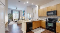 This single-floor residence showcases a thoughtfully designed open-concept layout where the kitchen flows seamlessly into the living area. The kitchen is equipped with warm honey-toned wood cabinetry, granite countertops, a mosaic tile backsplash, black appliances including a range, built-in microwave, refrigerator, and dishwasher, all set atop rich dark hardwood flooring. A peninsula with a double sink and additional counter space enhances both functionality and connectivity to the living area.

The living room is bright and welcoming, featuring soaring ceilings, a ceiling fan, large windows that invite ample natural light, and hardwood flooring that continues from the kitchen. The space is accented by a vibrant gallery wall arrangement, adding a bold artistic focal point.

Both bedrooms offer plush carpeted flooring and generous natural light through well-positioned windows with elegant draping. The primary bathroom is particularly notable for its dual-sink granite vanity, large wall mirror, walk-in closet, and a shower-tub combination. The secondary bathroom mirrors the same quality finishes, featuring a single granite vanity, tiled tub-shower, and tile flooring. Together, the rooms create a cohesive, comfortable, and stylish living environment.