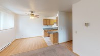 Located at 1717 40th St S in Fargo, North Dakota, this single-floor residence offers a practical and comfortable layout with a clean, neutral aesthetic throughout. The galley-style kitchen is well-appointed with warm oak cabinetry, dark granite-style countertops, a double sink, and white appliances including a range, refrigerator, and over-the-range microwave. Light hardwood-style flooring runs through the kitchen, while plush carpet covers the living, dining, and bedroom areas. The open living and dining space is bright and welcoming, featuring a chandelier accent in the dining area and a sliding glass door that provides access to the outdoors and fills the room with natural light. A wall-mounted air conditioning unit and baseboard heating ensure year-round comfort. The bedrooms are generously sized with large windows overlooking green outdoor surroundings and feature textured ceilings and baseboard heating. The full bathroom includes a tub and shower combination, a vanity with a framed mirror, and tile flooring. An additional vanity area with sink is accessible from the primary bedroom, complemented by a walk-in closet. Throughout the space, warm wood trim accents and neutral tones create a cohesive and functional living environment.