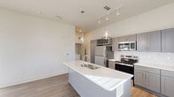 This two-story home in Huntsville, Alabama offers three bedrooms, three bathrooms, and a thoughtfully designed layout spread across two well-proportioned floors. The main level features a contemporary kitchen equipped with stainless steel appliances, gray shaker-style cabinetry, a herringbone tile backsplash, and a large center island with a double sink and white quartz countertops. Glass pendant lights and a track lighting system illuminate the space, which flows openly toward the main entrance, where multiple windows allow generous natural light into the living area. Wood-look plank flooring runs throughout the main living spaces, adding warmth and continuity. The attached two-car garage includes an automatic opener and a side window for added natural light, with interior access doors providing convenient entry. Upstairs, the bedrooms are finished with the same wood-look flooring and feature ceiling fans and closets, including a walk-in closet in one of the rooms. The primary bedroom is a comfortable, well-lit space. The bathrooms are finished with gray vanity cabinetry, white quartz countertops, and tile surrounds. A dedicated laundry area is also present. The overall aesthetic is clean, modern, and move-in ready.