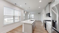 Located at 300 Main St in Madison, NJ, this thoughtfully designed 2-bedroom, 2-bathroom residence offers a clean, modern aesthetic throughout its single-floor layout. Light hardwood flooring flows seamlessly across the living areas, complemented by crisp white walls and recessed lighting that create a bright, airy atmosphere. The open-concept kitchen, dining, and living area serves as the heart of the home, anchored by a large center island with a white quartz countertop, undermount sink, and elegant pendant lighting. The kitchen is outfitted with shaker-style cabinetry in a soft gray finish, a herringbone tile backsplash, and a full suite of stainless steel appliances including a gas range and French door refrigerator. Multiple windows throughout the space invite abundant natural light. Both bedrooms are generously sized, featuring light hardwood floors and wide windows with outdoor views. The spacious primary bedroom includes its own en-suite bathroom complete with a double-sink vanity, large-format tile flooring, and a glass-enclosed walk-in shower. A well-appointed second bathroom mirrors the same refined finishes. The residence also includes five closets for exceptional storage and a dedicated in-unit laundry area, rounding out a highly functional and polished living space.