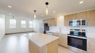 Located at 547 River St in Troy, NY, this modern two-story residence offers a thoughtfully designed layout spread across two levels. The main floor is anchored by a generous open-plan kitchen and living area, flooded with natural light from a row of tall windows that frame views of the surrounding neighborhood. The kitchen is appointed with warm wood-toned cabinetry, crisp white quartz countertops, a central island with pendant lighting, and a full suite of stainless steel appliances including a range, microwave, dishwasher, and refrigerator — all combining to create a clean, contemporary aesthetic. The upper level houses the spacious primary bedroom, featuring plush carpeting, a window with views of the Troy skyline, and access to two closets for ample storage. The full bathroom includes a walk-in shower and is conveniently positioned near a dedicated in-unit laundry closet with stacked washer and dryer. Additional highlights include soaring vaulted ceilings with exposed ductwork lending an industrial-chic character, a private balcony, a hallway connecting key spaces, and a staircase with natural wood treads. The overall palette of crisp whites and neutral tones creates a bright, airy atmosphere throughout.