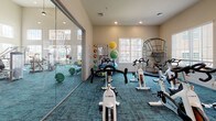 Located on Carl D Silver Parkway in Fredericksburg, Virginia, this single-floor fitness center is a comprehensively outfitted facility designed to support a wide range of workout routines. The main cardio floor impresses with soaring ceilings, pendant lighting, and large windows that flood the space with natural light. Rows of TRUE-brand treadmills, ellipticals, and recumbent bikes are arranged across teal-toned carpet, with multiple wall-mounted televisions keeping users entertained during their sessions. Full-length mirrors line the walls, amplifying the sense of openness throughout.

A dedicated free weights area features a complete dumbbell rack, barbells with weight plates, and floor-to-ceiling mirrors, providing ample space for strength training. Adjacent to this is a functional training zone with rubber flooring, a cable machine, battle ropes, plyo boxes in varying heights, stability balls, and a wall-mounted TV, making it ideal for high-intensity and cross-training workouts.

A separate cycling studio houses multiple TRUE spin bikes on vibrant teal carpet, with a glass partition offering views into the main gym floor. Natural light enters through a glass exterior door, creating an energizing environment. Throughout the facility, the design maintains a clean, modern aesthetic with neutral walls, recessed lighting, and thoughtful equipment placement that maximizes usability and flow.