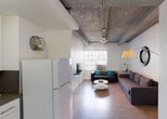 Located on iconic Collins Avenue in the heart of Miami Beach, this single-floor unit showcases an industrial-inspired aesthetic defined by its distinctive exposed concrete beam ceilings, which lend an urban character throughout the space. Wood-look tile flooring runs seamlessly across the main areas, creating a cohesive and easy-to-maintain foundation.

The open-concept living area is generously proportioned, accommodating multiple seating arrangements including a large sectional sofa and a leather couch, centered around a round white coffee table. Natural light filters in through windows fitted with vertical blinds and wall-mounted AC units, keeping the space bright and comfortable.

The kitchen is efficiently designed with white cabinetry, a gas range, microwave, and a full-size refrigerator, complemented by a small dining area near the entry door. The layout makes smart use of available space while maintaining functionality.

The bedroom features the same signature exposed beam ceiling and is equipped with a window with an AC unit, providing a private and restful retreat. The full bathroom includes a tub-shower combination with a curtain, toilet, and vanity, finished in clean, neutral tones.

The unit's location on Collins Ave places it steps from Miami Beach's world-renowned beaches, dining, and entertainment.