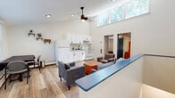 Located in Hartford, CT (06105), this two-floor residential space offers a clean, modern aesthetic throughout. The main living area is an open-concept design that combines a fully equipped kitchen and a comfortable living room. The kitchen features white cabinetry, a refrigerator, and a gas range, complemented by light hardwood-style flooring. A striking double-height ceiling with clerestory windows floods the space with natural light, while a ceiling fan adds both function and style. A built-in bar-height counter separates the kitchen from the living area, which includes plush seating and a wood coffee table.

The second living area, located on another level, provides additional seating with direct access to an entry door and exterior views. Multiple bedrooms are spread across the two floors, each featuring hardwood-style flooring, windows with views of surrounding greenery, and baseboard heating. The bedrooms offer a quiet, comfortable retreat with ample natural light.

Two bathrooms serve the space. One presents a classic look with a black-and-white mosaic tile floor and subway tile wainscoting, while the other includes a full bathtub with shower. Together, the rooms create a functional and well-appointed multi-room layout suited for shared or multi-occupant living.