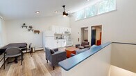 Located in Hartford, CT (06105), this two-floor residential space offers a clean, modern aesthetic throughout. The main living area is an open-concept design that combines a fully equipped kitchen and a comfortable living room. The kitchen features white cabinetry, a refrigerator, and a gas range, complemented by light hardwood-style flooring. A striking double-height ceiling with clerestory windows floods the space with natural light, while a ceiling fan adds both function and style. A built-in bar-height counter separates the kitchen from the living area, which includes plush seating and a wood coffee table.

The second living area, located on another level, provides additional seating with direct access to an entry door and exterior views. Multiple bedrooms are spread across the two floors, each featuring hardwood-style flooring, windows with views of surrounding greenery, and baseboard heating. The bedrooms offer a quiet, comfortable retreat with ample natural light.

Two bathrooms serve the space. One presents a classic look with a black-and-white mosaic tile floor and subway tile wainscoting, while the other includes a full bathtub with shower. Together, the rooms create a functional and well-appointed multi-room layout suited for shared or multi-occupant living.