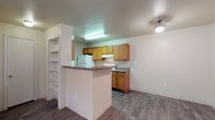 This single-story unit is designed with a functional, open layout that connects the living area directly to the kitchen. The living space features dark wood-look flooring and a ceiling fan with integrated lighting, creating a practical and comfortable environment. Natural light enters through windows fitted with blinds, and a dedicated entry door provides direct access to the space.

The kitchen is well-equipped with warm-toned wood cabinetry lining both sides of the galley-style workspace, granite-look countertops, a white gas range, refrigerator, and sink. A peninsula counter separates the kitchen from the living area and offers additional prep space. Adjacent to the kitchen, built-in open shelving provides convenient storage.

A hallway connects the bedrooms and bathrooms. The bedrooms include both carpeted and wood-look flooring options, with ceiling fans, windows for natural light, and ample wall space. Two full bathrooms are present, each featuring a tub-shower combination, toilet, vanity with sink, and wood-look flooring. The overall palette is neutral throughout, with light walls and clean finishes contributing to a cohesive, move-in-ready atmosphere.