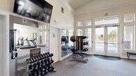 This fitness center is thoughtfully designed to support a comprehensive workout experience across multiple interconnected zones. The main exercise area features soaring vaulted ceilings with crown molding, lending the space an open, airy quality that enhances the sense of scale. Neutral-toned walls and plush carpet flooring create a clean, welcoming environment throughout.

The free weights zone is well-stocked with a full rack of dumbbells in graduated sizes, complemented by an adjustable weight bench and a multi-functional cable and resistance machine. Medicine balls and resistance bands add versatility to strength training options. A large wall mirror reflects natural light and assists with form checking during workouts.

An adjoining cardio section houses multiple treadmills, an elliptical trainer, and additional cardio equipment, all positioned to take advantage of the natural light streaming through large windows. A wall-mounted flat-screen television accompanies this area for entertainment during workouts.

Large double glass doors open directly to an outdoor pool area, providing refreshing views and easy access to exterior amenities. The facility also includes a restroom and a water station for convenience. Abundant windows throughout ensure the space remains bright and connected to the outdoors, creating an inviting atmosphere for daily fitness routines.