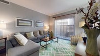 This single-floor residence offers a cohesive and thoughtfully designed layout with modern finishes and a neutral color palette throughout. The living room serves as the centerpiece of the space, featuring crown molding, dark hardwood-style flooring, and a large sliding glass door with vertical blinds that invites abundant natural light and provides access to an outdoor area. The room comfortably accommodates a sectional sofa and accent seating, anchored by a geometric-patterned area rug in soft green tones.

Adjacent to the living area is a dedicated dining space with the same rich hardwood-style flooring, crown molding, and ample wall space for artwork — ideal for intimate gatherings. The galley-style kitchen is efficiently designed with gray shaker cabinetry, white countertops, dark wood-look flooring, a stone-tile backsplash, and stainless steel appliances including a dishwasher and range.

The bedroom is a serene retreat with plush carpeting, a ceiling fan, natural light from a window with blinds and curtain panels, and generous closet space. The full bathroom features a vanity with a white countertop, dark cabinetry, dark wood-look flooring, and a tub-shower combination, delivering a clean and functional design.