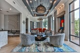 Located along Atlanta Student Movement Boulevard SW in Atlanta, Georgia, this thoughtfully designed single-floor amenity space combines contemporary aesthetics with functional versatility. The open-plan layout is anchored by a spacious lounge area finished with wide-plank hardwood flooring, bold abstract area rugs in teal, gold, and charcoal, and plush swivel accent chairs with gold-toned bases. A striking geometric pendant light fixture hangs overhead, complementing the dark tray ceilings that add architectural depth and contrast to the bright white walls.

A built-in wet bar with a beverage refrigerator, a mosaic tile backsplash in shades of navy and white, and a granite countertop serves as a stylish focal point. Adjacent private offices or co-working nooks provide dedicated workspace, outfitted with task chairs and accent lighting panels.

The lounge flows into a vibrant gathering area with a colorful built-in bench nook featuring a bold primary-colored panel backdrop and floor-to-ceiling windows on multiple sides, flooding the interior with natural light and offering views of the surrounding greenery. A separate private dining room showcases a live-edge wood table surrounded by upholstered terracotta chairs, illuminated by an industrial-style chandelier and framed by large black-framed windows. French doors connect the spaces seamlessly, creating an inviting and cohesive environment throughout.