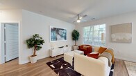 This thoughtfully designed single-floor residence offers a seamless blend of modern aesthetics and functional living. The open-concept layout connects the living, dining, and kitchen areas, creating an inviting and cohesive flow throughout the space. Warm hardwood-style flooring runs consistently throughout, tying each room together.

The living area is bright and airy, featuring large windows with exterior views, a ceiling fan, and ample room for comfortable seating arrangements. Adjacent to it, the kitchen stands out with two-tone cabinetry — dark lower cabinets paired with white uppers — a mosaic tile backsplash, stainless steel appliances, and a generous island with a waterfall countertop illuminated by geometric pendant lighting. A dining area sits nearby, benefiting from the same natural light.

The bedroom is calm and well-proportioned, with a large window allowing in abundant natural light and views of the surrounding exterior. The primary bathroom impresses with dual-sink vanity, dark cabinetry with ample storage, a soaking tub with tile surround, and direct access to a walk-in closet. A secondary bathroom features a tub-shower combination with large-format tile.

The entry hallway, accented by recessed lighting and clean white millwork, provides a polished welcome to the residence.