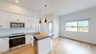 This well-designed upper-floor unit presents a thoughtfully arranged open-concept layout finished in a clean, contemporary style. The main living area is anchored by light-toned hardwood flooring that flows seamlessly from the kitchen through to the living space, creating a bright and cohesive atmosphere. A wall-mounted mini-split system provides climate control throughout.

The kitchen is a standout feature, equipped with white shaker cabinetry, a subway tile backsplash, and dark countertops that extend across a central island with an integrated sink. Stainless steel appliances include a range, microwave, dishwasher, and refrigerator. Two matte black pendant lights hang above the island, adding a modern accent. The entry door features a keypad lock for added convenience.

The bedroom is carpeted for comfort and includes a wall-mounted mini-split unit. A window frames views of the surrounding neighborhood and distant mountains, filling the room with natural light. The bathroom features a floating white vanity with dark countertop, a large mirror, built-in shelving, and hardwood-style flooring.

A private balcony extends off the main living area, offering open views of the neighborhood rooftops and a picturesque mountain backdrop under expansive skies.