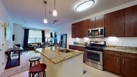 This single-story residence offers a thoughtfully designed open-concept layout that connects the kitchen, dining, and living areas into one cohesive space. The kitchen is a standout feature, showcasing rich dark-wood cabinetry extending to the ceiling, granite countertops, and a full suite of stainless steel appliances including a gas range, microwave, refrigerator, and dishwasher. A central island with an undermount sink and bar seating provides additional prep space and a natural gathering point. Light tile flooring and pendant lighting complete the kitchen's polished look.

The living area is carpeted and generously sized, with large windows dressed in dark drape panels that frame outdoor views and allow ample natural light. The space accommodates comfortable seating and entertainment furnishings with ease.

Two bedrooms offer carpeted floors and sizable windows. The primary bedroom features an accent wall in deep teal, adding a bold design element, while the secondary bedroom provides a more neutral, versatile setting. Both rooms include closet access.

The bathroom is finished with travertine-style tile, a granite-topped vanity with dark wood cabinetry, and a full soaking tub with shower. Conveniently adjacent is a stacked in-unit washer and dryer, adding practical functionality to the overall layout.