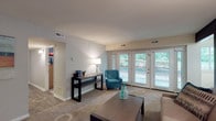 Located at 3831 Brentwood Rd in Raleigh, NC, this single-floor residence offers a well-organized layout designed for comfortable everyday living. The spacious living room features plush carpeting, neutral walls, and large French doors that flood the space with natural light and offer views of the surrounding greenery. A secondary living or sitting area is also present, finished with soft gray tones, carpet flooring, and tasteful décor that creates a relaxed atmosphere. The kitchen is equipped with white cabinetry, granite-style countertops, black appliances including a range and refrigerator, and wood-look flooring that adds warmth to the functional space. Adjacent to the kitchen, the dining area accommodates a full-sized table beneath a modern chandelier, with a large window overlooking the wooded exterior. The bedrooms include carpeted floors and ample closet space; one bedroom features a charming castle-themed wall mural, while another offers a bright window and a dedicated study area. Both bathrooms are finished with white cabinetry, granite-style countertops, and wood-look tile flooring, providing a clean and practical design. Throughout the home, consistent finishes and abundant natural light contribute to a cohesive and inviting living environment.