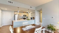 Located on the third floor at 696 Whitney Rd W in Fairport, NY, this well-appointed unit offers a thoughtfully designed single-level layout that maximizes both comfort and functionality. The open-concept main living area seamlessly connects the kitchen, dining, and living spaces, creating an inviting flow ideal for everyday living and entertaining. The kitchen is equipped with stainless steel appliances — including a full-size refrigerator, microwave, and range — complemented by light wood cabinetry and a generous peninsula with a clean white countertop and pendant lighting overhead. The dining area accommodates a full dining table set, positioned just steps from the kitchen for convenience. The living room features large windows that invite natural light and offer outdoor views, along with a door leading to a private balcony. Hardwood-style flooring runs throughout the main living spaces, transitioning to plush carpet in the bedrooms. Both bedrooms are comfortably sized with large windows, neutral soft-tone walls, and ample natural light. The unit's soft gray-green color palette and clean finishes lend a calm, modern ambiance throughout.