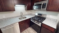 This single-floor residence offers a thoughtfully designed living space centered around a standout kitchen. The kitchen is finished with rich, dark espresso-toned wood cabinetry that extends from floor to ceiling, providing generous storage throughout. Light-toned granite countertops with subtle speckled detailing contrast beautifully against the dark cabinetry, lending an elegant and timeless aesthetic to the space. A stainless steel undermount sink with a modern pull-down faucet is seamlessly integrated into the countertop, complemented by under-cabinet lighting that illuminates the workspace below. The kitchen is fully equipped with a full suite of stainless steel appliances, including a gas range with multiple burners, an over-the-range microwave, and a dishwasher — offering both style and everyday functionality. The flooring throughout features light wood-tone planks that add warmth and continuity to the space. The overall design of the kitchen strikes a balance between contemporary finishes and practical layout, making it a functional and visually appealing hub of the home. The cohesive color palette and quality finishes throughout reflect a well-maintained and move-in-ready residence.