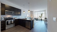 Located at 5300 S 76th St in Greendale, Wisconsin, this single-floor residence showcases a well-designed open-concept layout that seamlessly connects the kitchen, dining, and living areas. The kitchen is outfitted with dark espresso cabinetry, granite countertops, a subway tile backsplash, and stainless steel appliances, including a built-in microwave and dishwasher. A central island with an integrated sink and bar seating provides a functional and stylish focal point, illuminated by pendant lighting overhead.

The living area is generously proportioned, featuring durable wood-look flooring and floor-to-ceiling windows that flood the space with natural light and offer outdoor views. A sliding glass door provides direct access to an exterior space, enhancing the open, airy feel of the room.

The bedroom is carpeted for comfort and includes large windows that continue the natural light theme throughout the unit. The bathroom features consistent granite countertops atop dark vanity cabinetry, wood-look flooring, and clean, neutral wall tones that contribute to a cohesive modern aesthetic. Overall, the space presents a contemporary design with high-quality finishes and a bright, functional atmosphere.