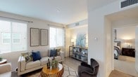 This single-floor residence offers a thoughtfully designed layout that balances open communal spaces with private retreats. The living room serves as the heart of the home, featuring light wood-style flooring, clean white walls, and recessed lighting that creates a bright, welcoming atmosphere. A generous sectional seating area and a stylish organic-shaped coffee table anchor the space, while framed artwork adds a curated touch.

The kitchen is outfitted with dark cabinetry, stainless steel appliances including a gas range and built-in microwave, and a light-toned countertop island. A window above the countertop area allows natural light to filter in, with views of the surrounding landscape. Adjacent to the kitchen, a dedicated dining nook features large windows on two walls, filling the space with natural light and offering pleasant outdoor views.

The primary bedroom is generously proportioned, with plush carpeting, a ceiling fan, and a window that brings in natural light. It connects to a hallway leading to a well-appointed en-suite bathroom. A secondary bedroom offers similar comfort with carpeted flooring and a ceiling fan.

The bathroom features wood-look tile flooring, a dark vanity with a light countertop, and a framed mirror. Throughout the residence, the consistent use of neutral tones and modern finishes creates a cohesive and inviting aesthetic.