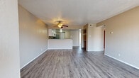 This single-floor unit offers a practical and well-organized layout highlighted by wood-look plank flooring that runs throughout the entire space, lending a clean and cohesive aesthetic. The open-concept living area is spacious and airy, anchored by a ceiling fan overhead and textured ceilings. A half-wall peninsula separates the living area from the kitchen, creating a natural flow while maintaining a sense of openness.

The kitchen is well-appointed with white cabinetry, a mosaic tile backsplash, stainless steel appliances including a refrigerator and electric range, a double-basin sink set into the peninsula countertop, and a dishwasher. Additional storage is available via a dedicated pantry closet adjacent to the kitchen.

The living area opens to built-in open shelving, ideal for display or storage, and connects to a hallway leading to the bedrooms. Each bedroom features neutral-toned walls, wood-look flooring, and windows with blinds that allow natural light to filter in. At least one bedroom includes a walk-in closet with built-in rod, while another features a standard reach-in closet. The overall color palette of warm beige tones and white trim creates a neutral, move-in-ready environment throughout the unit.