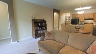 This two-floor home offers a comfortable and classic living environment with a warm, inviting ambiance throughout. The main living area is finished with plush wall-to-wall carpeting and painted in soft, neutral tones that create a relaxed and welcoming atmosphere. A traditional wooden bookcase, filled with books and accented by a decorative globe, anchors the space and adds a scholarly charm. Comfortable upholstered seating, including a sofa dressed with a floral accent pillow, provides an ideal setting for relaxation. An arched interior doorway adds an elegant architectural detail, leading through to additional living spaces including what appears to be a dining or kitchen area visible in the background. The open sightlines between rooms enhance the sense of connectivity and flow across the floor plan. Clean white baseboards and neutral walls provide a timeless backdrop that complements the traditional furnishings. The second floor adds additional living space, contributing to the home's generous and functional layout. Overall, this residence combines classic design elements with practical comfort, making it a warm and well-appointed home suited to everyday living.