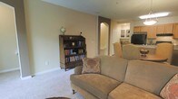 This two-floor home offers a comfortable and classic living environment with a warm, inviting ambiance throughout. The main living area is finished with plush wall-to-wall carpeting and painted in soft, neutral tones that create a relaxed and welcoming atmosphere. A traditional wooden bookcase, filled with books and accented by a decorative globe, anchors the space and adds a scholarly charm. Comfortable upholstered seating, including a sofa dressed with a floral accent pillow, provides an ideal setting for relaxation. An arched interior doorway adds an elegant architectural detail, leading through to additional living spaces including what appears to be a dining or kitchen area visible in the background. The open sightlines between rooms enhance the sense of connectivity and flow across the floor plan. Clean white baseboards and neutral walls provide a timeless backdrop that complements the traditional furnishings. The second floor adds additional living space, contributing to the home's generous and functional layout. Overall, this residence combines classic design elements with practical comfort, making it a warm and well-appointed home suited to everyday living.
