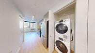 Located on the sixth floor at 351 Marin Blvd in Jersey City's vibrant waterfront district, this one-bedroom, one-bathroom unit offers a well-designed layout with a clean, modern aesthetic throughout. Light hardwood flooring flows seamlessly across the open living and kitchen areas, creating a warm and cohesive atmosphere.

The galley-style kitchen is thoughtfully appointed with sleek grey cabinetry extending to the ceiling for generous storage, white subway tile backsplash, dark countertops, and a full suite of stainless steel appliances including a range, microwave, and refrigerator. Recessed and linear lighting illuminates the kitchen efficiently.

The bedroom is a comfortable, well-proportioned space featuring large floor-to-ceiling windows that frame striking views of the Jersey City urban skyline, filling the room with abundant natural light. A wall-mounted HVAC unit provides climate control.

The bathroom maintains the unit's clean design language, finished with large-format neutral floor tiles, a light wood vanity with mirror cabinet, and bright overhead lighting.

Crisp white walls throughout, combined with natural light and warm flooring, give the unit a bright and airy feel that maximizes its efficient footprint — making it an ideal urban residence in one of New Jersey's most sought-after neighborhoods.