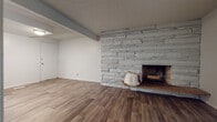 This single-floor unit offers a thoughtfully laid-out interior with a mix of practical finishes and notable design elements. The living area serves as a focal point of the space, anchored by a floor-to-ceiling stacked-stone fireplace with a raised hearth, adding texture and character to the room. Wood-look plank flooring runs throughout the main living and kitchen areas, complementing the neutral white walls and textured ceiling.

The kitchen is equipped with stainless steel appliances, including a refrigerator, range, and over-the-range microwave. White shaker-style cabinetry provides ample storage, while the wood-look flooring continues seamlessly from the living space, creating a cohesive flow.

A separate room, accessible from the main living area, features large vertical-blind-covered windows that allow natural light to filter in, making it a versatile space. The bedrooms are finished with wall-to-wall carpet and vertical blinds, offering a comfortable, quiet environment.

The bathroom is clean and functional, featuring a white tub-shower combination with built-in shelving, a standard toilet, and wood-look flooring that ties the unit together. Textured ceilings are consistent throughout, adding a uniform finish to the overall space.