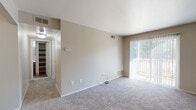 This single-floor residential unit offers a well-organized layout with a clear separation between living, sleeping, and functional spaces. The entry opens to a foyer with wood-style flooring, a coat closet, and direct sightlines into the main living area and kitchen beyond.

The living room is generously proportioned, featuring neutral-toned carpet, soft beige walls, and a large sliding glass door dressed with vertical blinds that allows abundant natural light and views of the surrounding greenery. A thermostat and multiple electrical outlets are conveniently positioned throughout.

The galley-style kitchen is efficiently designed with dark espresso cabinetry lining both sides, light-toned countertops, a stainless steel sink, and a stainless refrigerator. Wood-look flooring runs through this space, complementing the rich cabinetry tones and creating a cohesive, modern aesthetic.

The bedroom is a quiet, well-sized room with plush carpeting, neutral walls, and ample space for furnishings. A closet with shelving provides practical storage.

The bathroom is clean and functional, featuring a tiled tub-shower combination, a wood-vanity with a light countertop, a toilet, and wood-style flooring that ties in with the rest of the unit. Overall, the space presents a neutral, move-in ready palette with consistent finishes throughout.