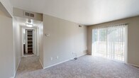 This single-floor residential unit offers a well-organized layout with a clear separation between living, sleeping, and functional spaces. The entry opens to a foyer with wood-style flooring, a coat closet, and direct sightlines into the main living area and kitchen beyond.

The living room is generously proportioned, featuring neutral-toned carpet, soft beige walls, and a large sliding glass door dressed with vertical blinds that allows abundant natural light and views of the surrounding greenery. A thermostat and multiple electrical outlets are conveniently positioned throughout.

The galley-style kitchen is efficiently designed with dark espresso cabinetry lining both sides, light-toned countertops, a stainless steel sink, and a stainless refrigerator. Wood-look flooring runs through this space, complementing the rich cabinetry tones and creating a cohesive, modern aesthetic.

The bedroom is a quiet, well-sized room with plush carpeting, neutral walls, and ample space for furnishings. A closet with shelving provides practical storage.

The bathroom is clean and functional, featuring a tiled tub-shower combination, a wood-vanity with a light countertop, a toilet, and wood-style flooring that ties in with the rest of the unit. Overall, the space presents a neutral, move-in ready palette with consistent finishes throughout.