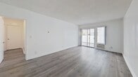 This 630-square-foot, one-bedroom, one-bathroom apartment is located at 318 S Almont Dr in the heart of Los Angeles, CA 90048. The single-floor layout is thoughtfully designed to maximize space and functionality throughout. The open-concept living room is bright and airy, featuring modern gray hardwood-style flooring, crisp white walls, and a textured ceiling. A sliding glass door floods the room with natural light and provides direct access to an outdoor area. A ceiling fan is positioned at the junction of the living and kitchen area, enhancing airflow throughout. The kitchen is efficiently designed with white cabinetry, granite countertops, stainless steel appliances including a built-in wall oven and refrigerator, and a tile floor. A peninsula with a double sink separates the kitchen from the living area. The 150-square-foot bedroom continues the hardwood-style flooring and features a wide mirrored sliding closet, a window for natural light, and clean white walls. The bathroom is well-appointed with a granite-topped vanity with white cabinetry, a large mirror, tile flooring, a toilet, and a combination soaking tub and glass-enclosed shower. A hallway connects the main rooms, completing this well-organized and modern urban residence.