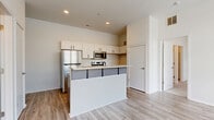 Located at 815 Kinnear Rd. in Columbus, Ohio, this single-floor, 2-bedroom, 1-bathroom unit offers a thoughtfully designed layout with modern finishes throughout. The open-concept kitchen serves as a central feature, showcasing white upper cabinetry, contrasting dark lower cabinets, a patterned tile backsplash, and granite countertops. A peninsula with bar seating provides both additional prep space and a casual dining area. Stainless steel appliances—including a refrigerator, range, microwave, and dishwasher—complete the well-appointed kitchen. Light wood-look flooring runs through the main living and kitchen areas, lending warmth and continuity to the space. Both bedrooms are carpeted and receive abundant natural light through large windows with exterior views. The spacious primary bedroom offers generous room to furnish comfortably. The full bathroom features wood-look flooring, a granite-topped vanity with white cabinetry, and access to a walk-in closet with built-in shelving. Two closets throughout the unit provide practical storage solutions. The clean, neutral color palette and recessed lighting create a bright, contemporary ambiance suited for modern living.
