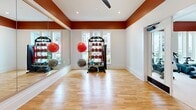 Located at 4101 Raleigh St in Charlotte, NC, this fitness center offers a comprehensive workout facility spread across a single, generously sized floor. The space is defined by a bold two-tone design, with rich terracotta-orange accent walls contrasting against crisp white ceilings and trim throughout, creating an energetic yet clean aesthetic. Large windows along the perimeter flood the main gym area with natural light while offering views of the surrounding exterior.

The main gym floor is expansive and well-organized, housing a wide array of cardio equipment including multiple treadmills, ellipticals, stair climbers, and a connected stationary bike with a digital display. Ceiling fans are installed throughout to maintain airflow and comfort. A multi-station cable and weight machine, along with a heavy bag and a full rack of kettlebells and dumbbells, cater to strength and functional training needs.

A separate studio room features polished hardwood flooring, floor-to-ceiling mirrors, a wall-mounted ballet barre, and an interactive smart mirror for guided workouts. This room also includes stability balls and medicine balls on a dedicated rack, making it ideal for yoga, stretching, or group fitness. The overall facility is thoughtfully designed to support a wide range of fitness activities in a bright, motivating environment.