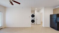 Located at 8800 Chad Colley Blvd in Fort Smith, Arkansas, this thoughtfully designed one-bedroom, one-bathroom unit offers a clean, modern aesthetic throughout its efficiently laid-out single floor. The open layout is anchored by light-toned tile flooring in the main living areas, complemented by crisp white walls and ceiling fans that enhance airflow and comfort.

The contemporary kitchen is a standout feature, showcasing light wood-grain cabinetry — both upper and lower — paired with white countertops, a stainless steel sink with a brushed nickel faucet, and a full suite of black appliances including a refrigerator, dishwasher, electric range, and microwave. The clean lines and ample cabinetry make this kitchen as functional as it is visually appealing.

The bedroom offers plush carpeting, a ceiling fan, and a window with blinds that brings in natural light. A dedicated closet provides practical storage. The bathroom features a tub/shower combination with a curved curtain rod, a white toilet, and a wood-toned vanity with a white countertop and black hardware accents — a cohesive and stylish finish.

A notable convenience is the in-unit stacked washer and dryer, neatly integrated into the living space. A hallway connects the rooms efficiently, completing this well-organized and modern unit.