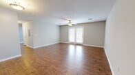 This well-appointed 3-bedroom, 2-bathroom apartment at Lakeshore Pointe in Brandon, MS offers a comfortable single-floor layout with thoughtful finishes throughout. The spacious living room is a standout, featuring rich hardwood-style flooring, a textured ceiling, a ceiling fan with light fixture, and French doors that invite natural light and provide outdoor access. The kitchen is equipped with stainless steel appliances — including a refrigerator, electric range, and over-the-range microwave — complemented by rich dark wood cabinetry and granite countertops, lending a polished, functional workspace. Both bathrooms continue the warm wood-style flooring and include full tub-shower combinations with clean white tile surrounds, dark wood vanity cabinetry, and granite countertops. The three bedrooms are carpeted for comfort, each featuring ceiling fans with light kits and neutral-toned walls that create a calm, versatile atmosphere. Natural light filters in through windows fitted with blinds. Consistent neutral wall tones and cohesive finishes throughout create a unified, move-in-ready feel across the entire home.