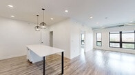 Located at 155 Jackson St in Oshkosh, WI, this modern 2-bedroom, 1-bathroom unit offers a thoughtfully designed open-concept layout with hardwood-style flooring throughout. The combined kitchen and living area serves as the heart of the space, featuring a sleek white kitchen with shaker-style cabinetry, a herringbone tile backsplash, stainless steel appliances including a refrigerator, range, microwave, and dishwasher, and a large white waterfall-edge island illuminated by stylish globe pendant lights. Recessed lighting enhances the bright, airy ambiance throughout. The spacious living area is framed by large black-framed windows that invite abundant natural light and offer views of the surrounding Oshkosh cityscape. Both bedrooms are well-proportioned with clean white walls and hardwood-style flooring; the primary bedroom includes a dedicated closet, while additional closets provide ample storage. A sliding barn door accents one of the secondary spaces, adding a modern industrial touch. The bathroom features a white vanity with undermount sink, black hardware accents, and wood-look flooring, maintaining the cohesive modern aesthetic. Exposed ductwork in the living area adds an urban, loft-inspired character to this clean, contemporary space.
