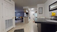 This single-floor unit offers a practical and cohesive layout centered around an open-concept living, dining, and kitchen area. The kitchen features light wood cabinetry, a peninsula with bar seating, tile flooring, and standard appliances including a refrigerator and dishwasher. The dining area sits adjacent to the kitchen, providing a natural flow for everyday use. The living room is carpeted and benefits from a sliding glass door that allows natural light to fill the space, complemented by a neutral gray accent wall and a textured ceiling.

The primary bedroom is carpeted and includes a closet, offering a calm and functional retreat. A second bedroom also features carpet and a window with views of surrounding greenery, bringing in additional natural light. Two bathrooms serve the unit, each featuring tile flooring and a tub-shower combination. The primary bathroom includes a wide vanity with dual sinks and an expansive mirror, while the secondary bathroom offers a single-sink vanity with ample cabinetry. Overall, the unit maintains a consistent, neutral aesthetic throughout.