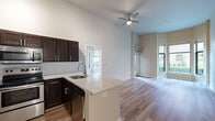 This well-appointed 2-bedroom, 2-bathroom residence is laid out on a single floor, offering an efficient and functional floor plan. The open-concept kitchen and living area serves as the heart of the home, highlighted by dramatically high ceilings and a ceiling fan that enhance the sense of spaciousness. The kitchen is outfitted with dark espresso cabinetry, white quartz countertops, a classic subway tile backsplash, and a full suite of stainless steel appliances including a refrigerator, range, microwave, and dishwasher. A peninsula island provides additional counter space and casual seating. Wood-style flooring flows consistently throughout the entire residence, lending a cohesive, modern aesthetic. The living area benefits from multiple windows that invite natural light and offer views of the surrounding exterior. The primary bedroom is generously sized and features tall ceilings, a large window, and access to a walk-in closet with wire shelving systems. The second bedroom also receives ample natural light. Both bathrooms are finished with dark wood vanities, white countertops, and tub-shower combinations. Two closets provide practical storage solutions throughout the home.